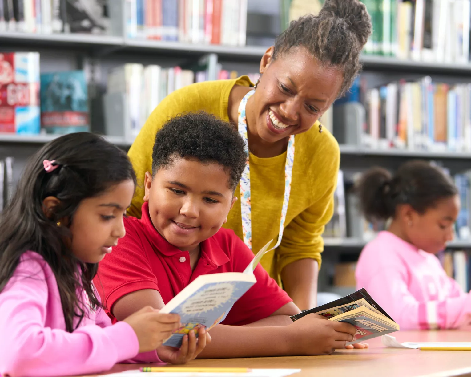 Librarian leans over seated students at the library who are reading a book